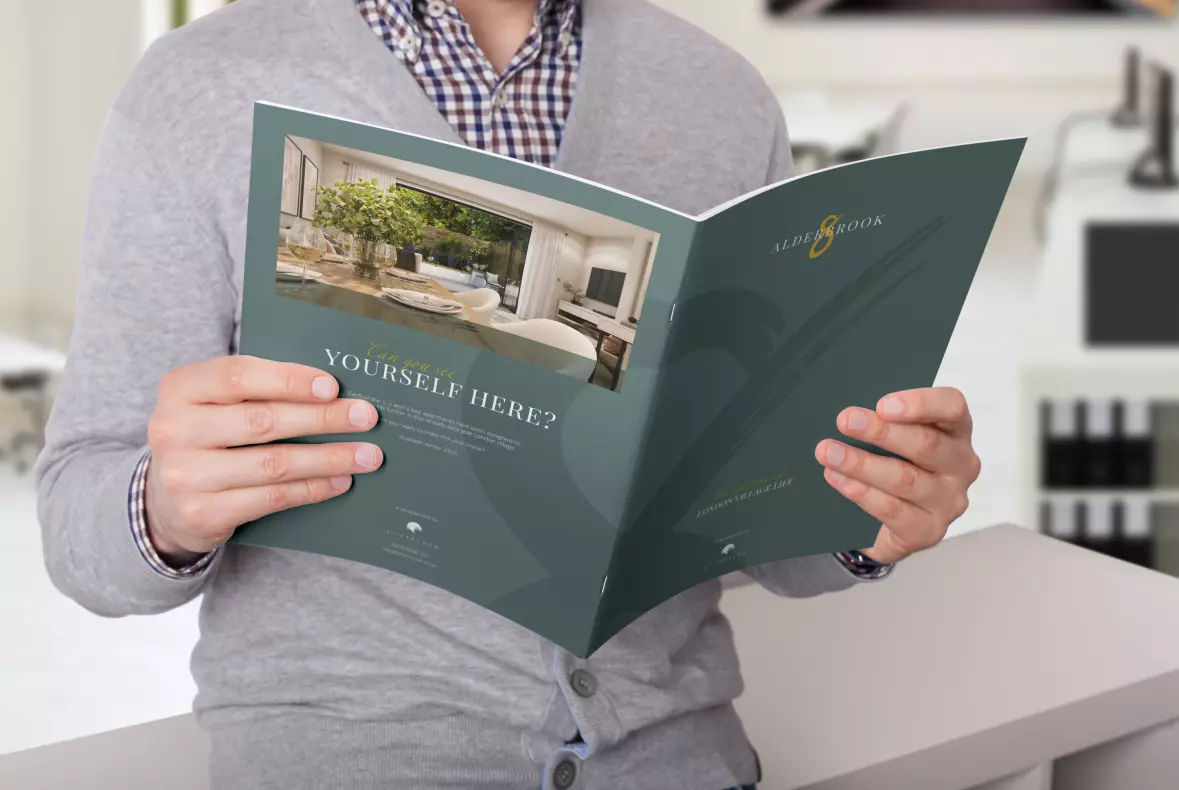 Picture of a man sitting on a desk holding the Alderbrook Road property brochure open and reading it