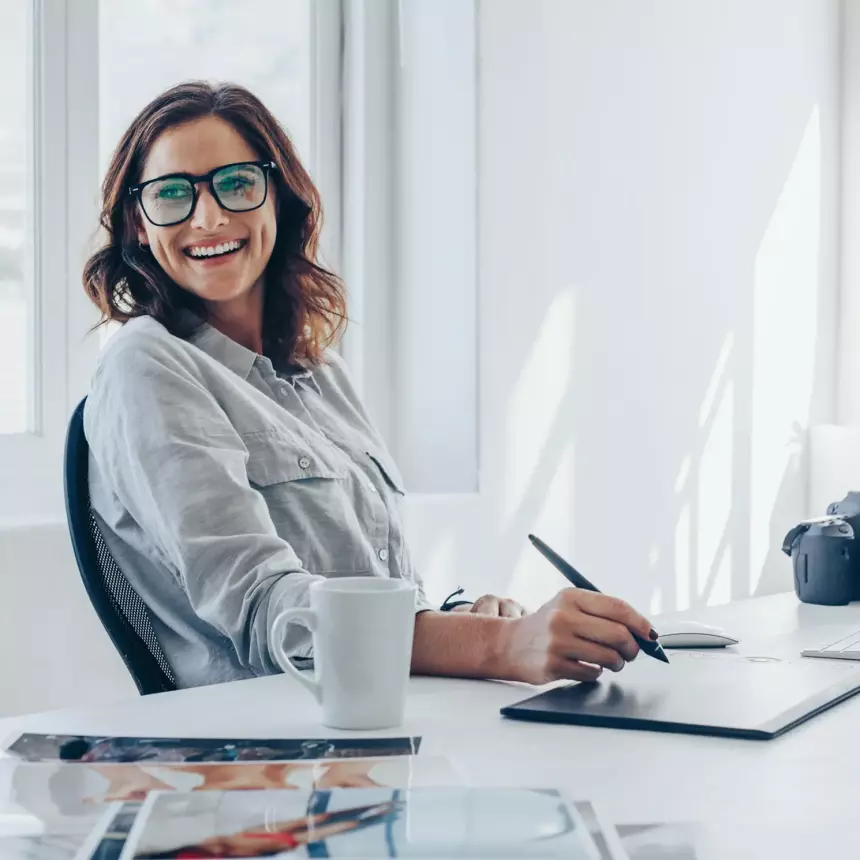 Lady designer in modern clean office using a drawing tablet to create some graphic design for the Estate Agency Industry, whilst leaning back in chair and smiling