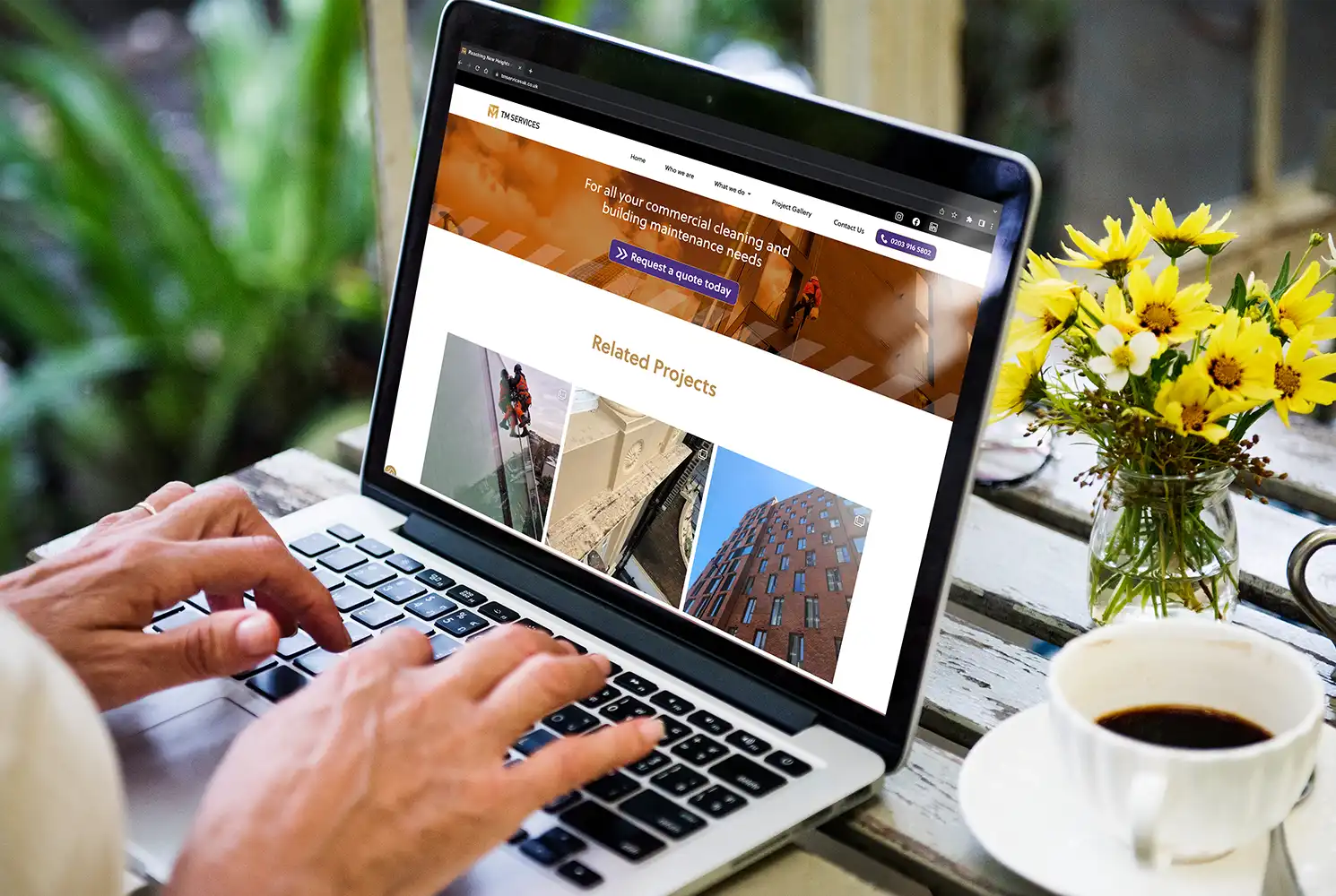 Image of a person checking out the TM Maintenance Services website on a Macbook whilst sat in a coffee shop